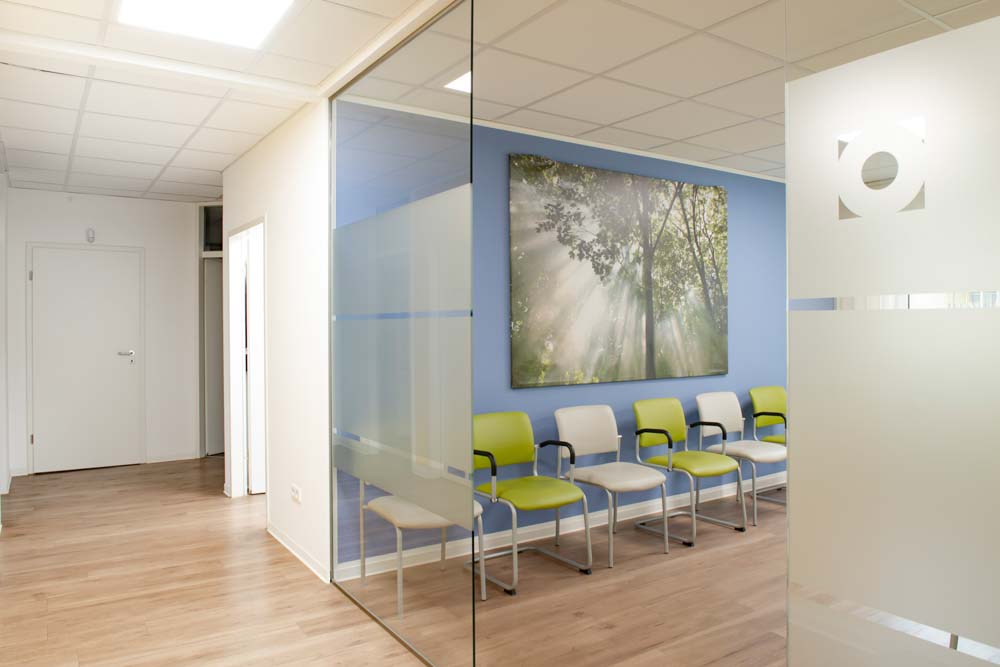 Heller Gang zwischen den Sprechzimmern, daneben die Glaswand zum Wartezimmer