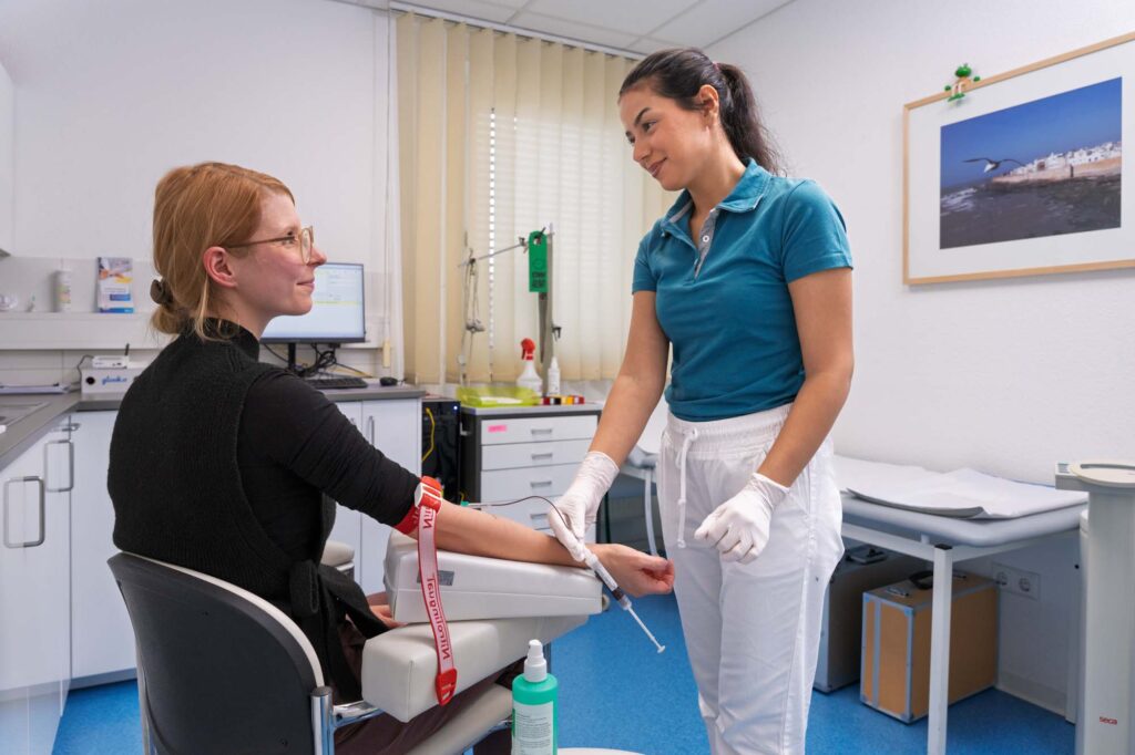 Eine Medizinische Fachangestellte nimmt einer sitzenden Patientin im Labor Blut ab