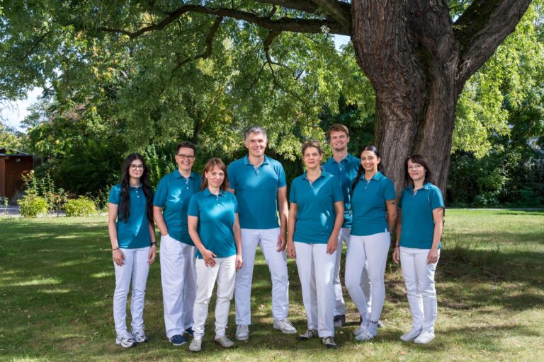 Gruppenfoto des Teams der Praxis Dr. Dimos im sonnigen Park unter einem Baum