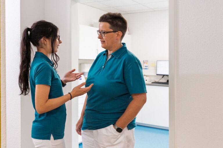 Eine Auszubildende und eine MFA im Gespräch vor der geöffneten Labortür